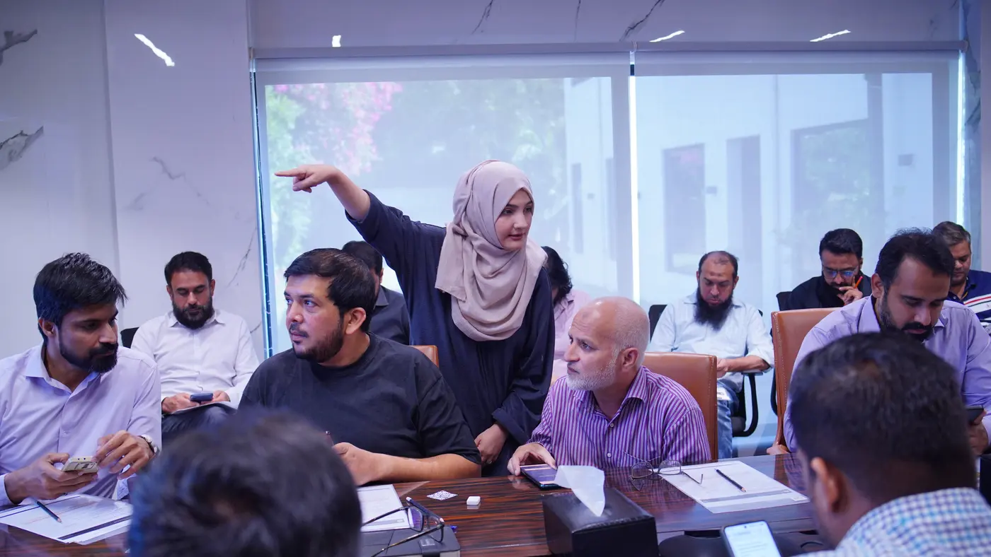 A facilitator standing among seated Amreli Steels leaders, pointing across the room during the discussion.