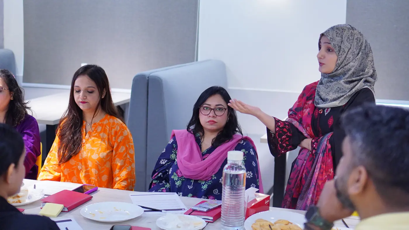 A facilitator in a patterned dress speaking to seated Jubilee Life colleagues.