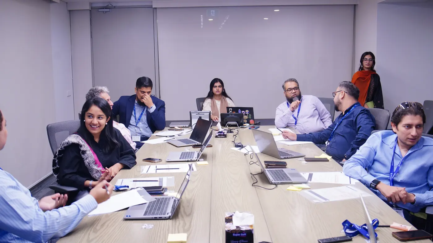 Standard Chartered colleagues with laptops open along a long conference table during the leadership session.