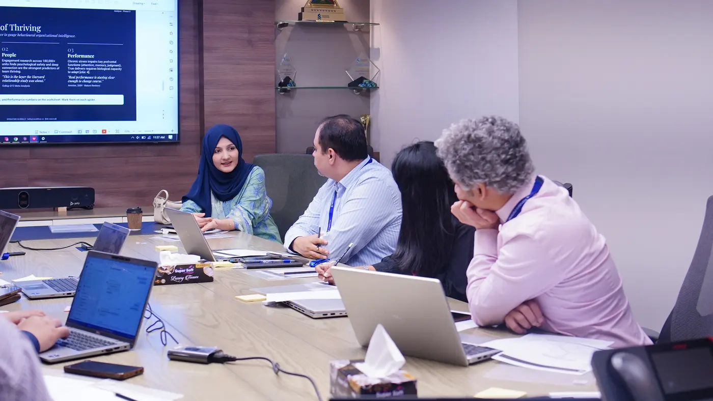 Standard Chartered colleagues seated in discussion, the facilitator at the head of the table and a screen behind them.